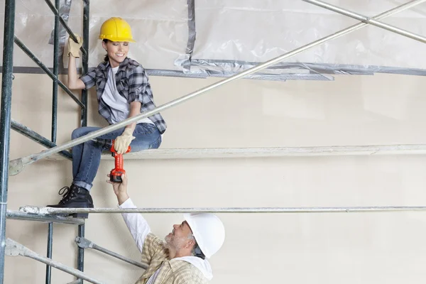 Architetto maschio che dà trapano al lavoratore femminile sul ponteggio in cantiere — Foto Stock