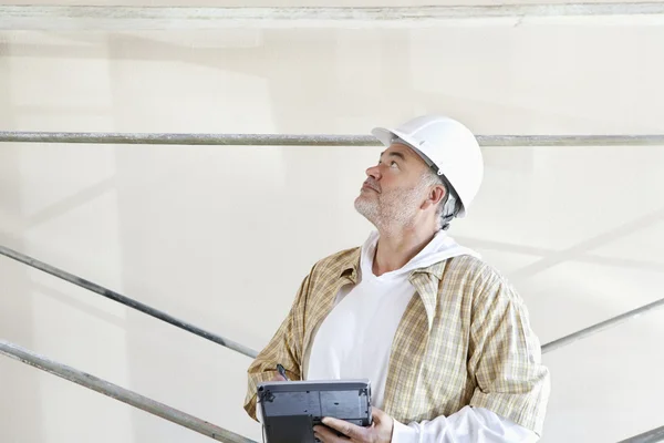 Architecte masculin mature faisant une note dans la tablette numérique tout en regardant vers le haut sur le chantier de construction — Photo