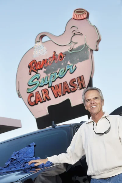 Portrait of mature owner of car wash standing below signboard with vehicle — Stock Photo, Image