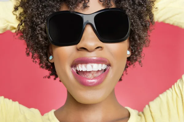 Close-up de uma mulher afro-americana alegre usando óculos de sol sobre fundo colorido — Fotografia de Stock