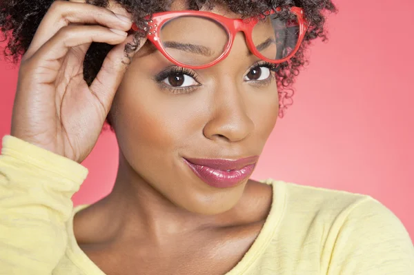 Retrato de uma mulher afro-americana segurando óculos retro sobre fundo colorido — Fotografia de Stock