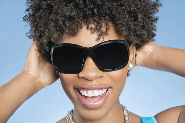 Close-up of cheerful young woman wearing sunglasses with hands behind head over colored background — Stock Photo, Image