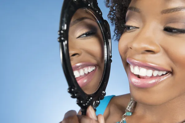 Close-up of a young woman looking at herself in mirror and smiling over colored background — Stock Photo, Image