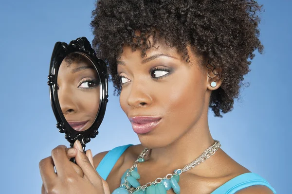 Close-up van Afro-Amerikaanse vrouw op zoek naar zichzelf in de spiegel over gekleurde achtergrond — Stockfoto