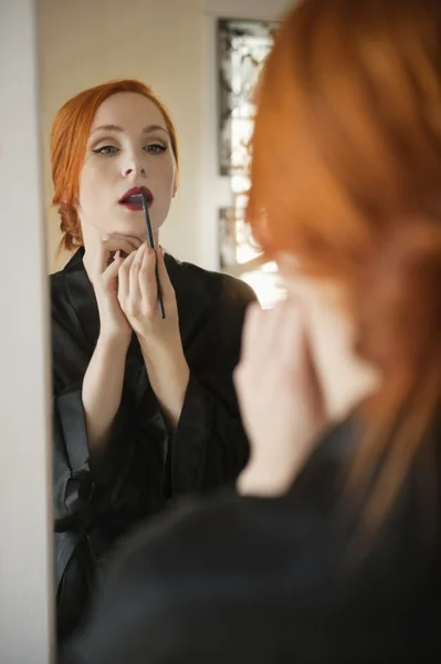 Young female applying lip liner in front of mirror — Stock Photo, Image