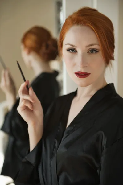 Retrato de uma bela mulher ruiva de roupão segurando um forro labial — Fotografia de Stock