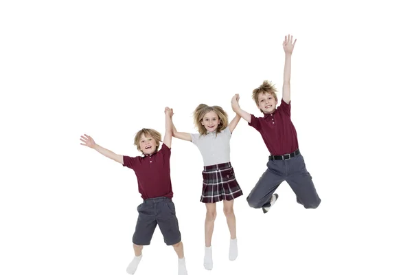 Portrait of happy school children holding hands while jumping over white background — Stock Photo, Image