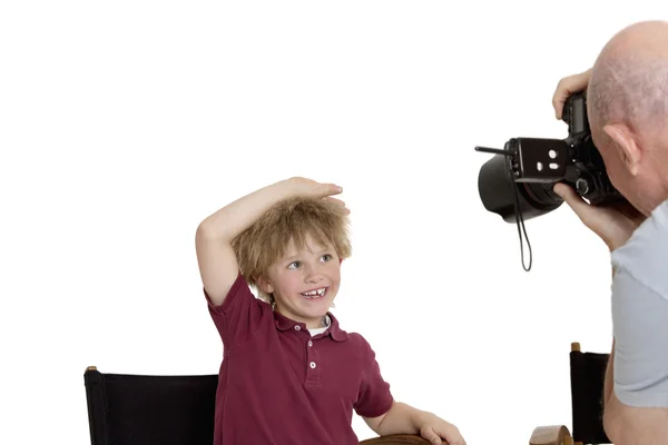 Senior photographer clicking school kid sitting on chair over white background — Stock Photo, Image