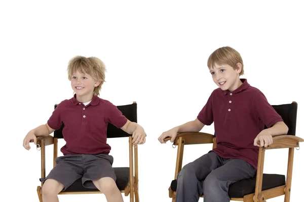 Two happy school kids sitting on director's chair over white background — Stock Photo, Image