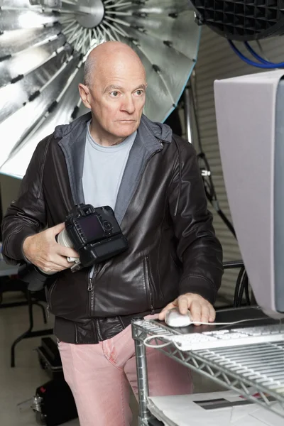 Senior photographer with camera using computer in studio — Stock Photo, Image
