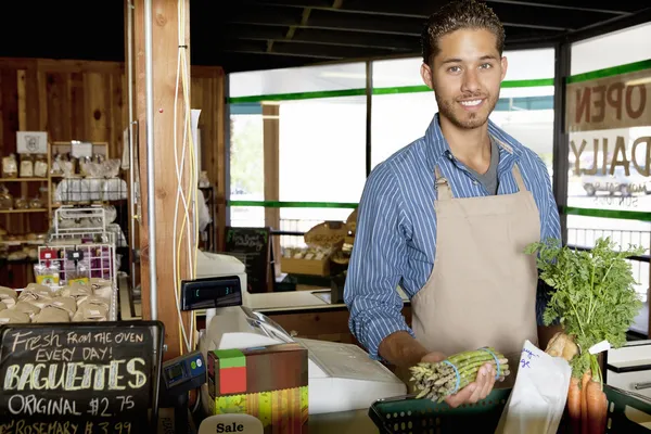 Portrait d'un beau jeune commis de magasin tenant des légumes dans un supermarché — Photo