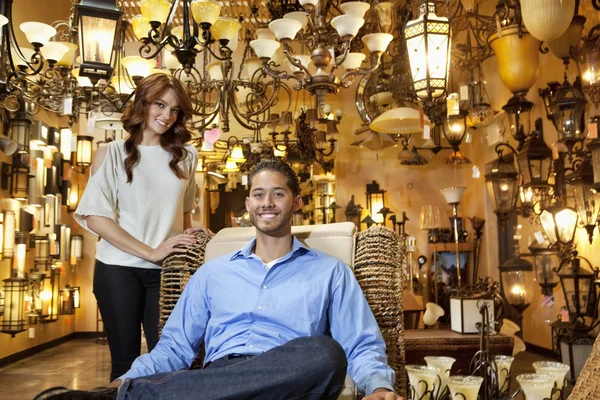 Portret van knappe jonge man zitten terwijl vrouw staande achtergrond in lichten winkel — Stockfoto