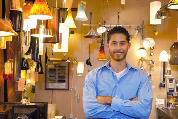 Portret van een gelukkig jonge man met armen gekruist in lichten winkel — Stockfoto