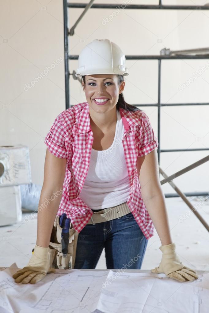 Portrait of a happy female construction worker wearing hardhat with blueprints