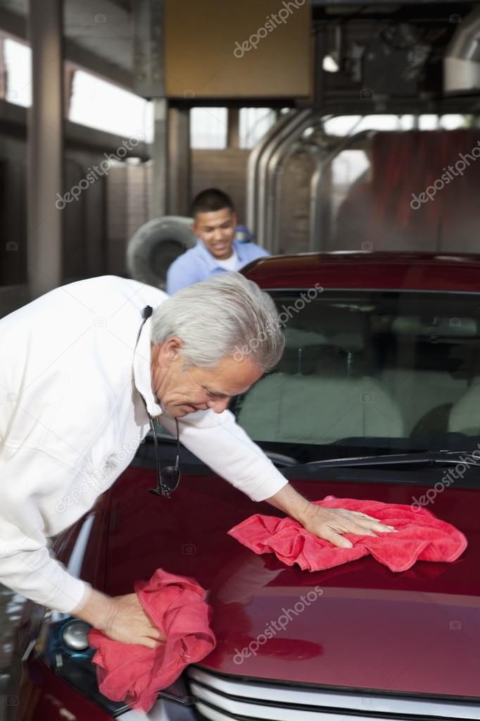 mature owner and young employee wiping vehicle with cloth in car wash