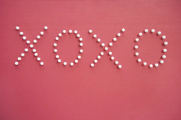 Close-up de alfinetes de pressão em formação de x e o sobre fundo rosa retratando abraços e beijos — Fotografia de Stock