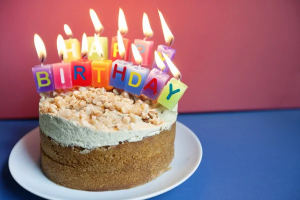 Close-up of candles burning on birthday cake over colored background — Stock Photo, Image