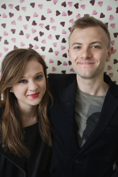 Portrait of beautiful young couple smiling over heart shaped wallpaper — Stock Photo, Image