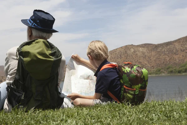 Grootvader en kleinzoon zitten met kaart op lakeside — Stockfoto