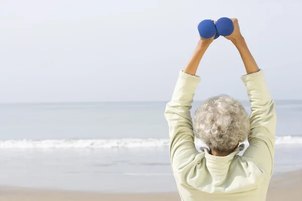 Seniorin übt mit Hanteln am Strand — Stockfoto