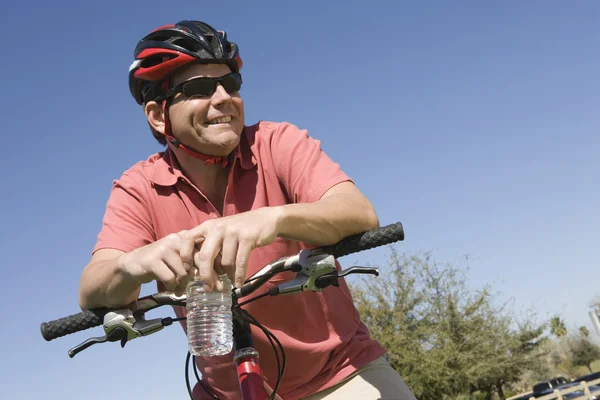 Мужчина-велосипедист с бутылкой воды против неба — стоковое фото
