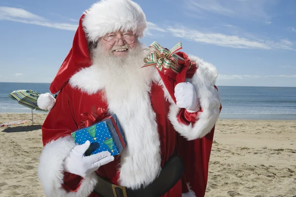 Father Christmas Stands With His Sack On Beach — Stock Photo, Image