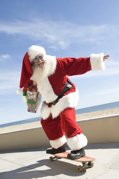 Santa claus skateboardingu s darem v ruce — Stock fotografie