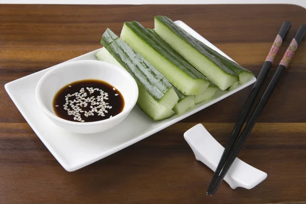 Molho de soja com fatias de pepino e pauzinhos na mesa — Fotografia de Stock