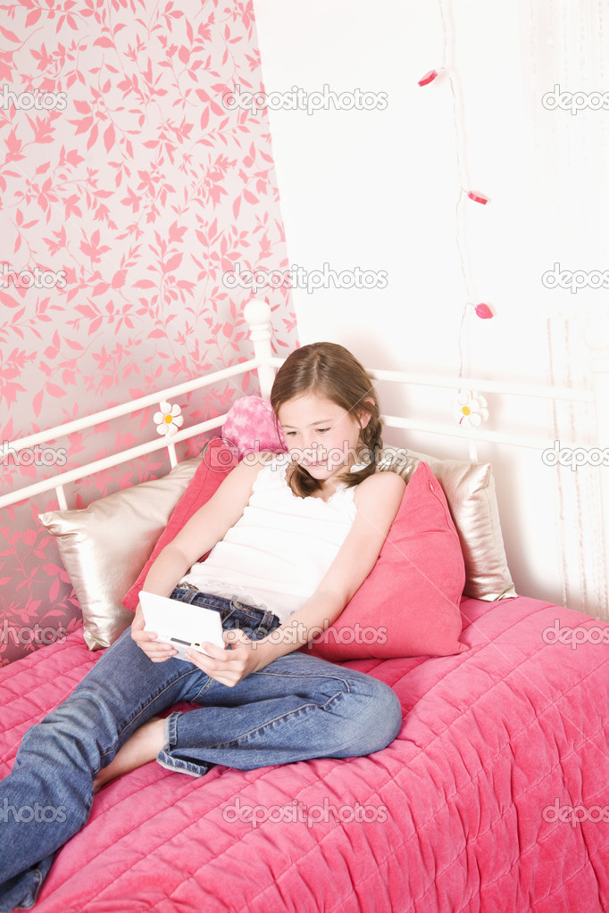 Young Girl In Bedroom Playing Handheld Game
