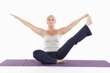 Mature woman sitting on mat and doing yoga with arms outstretched clipart
