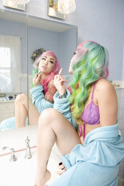 Young woman holding lipstick while looking into mirror — Stock Photo, Image