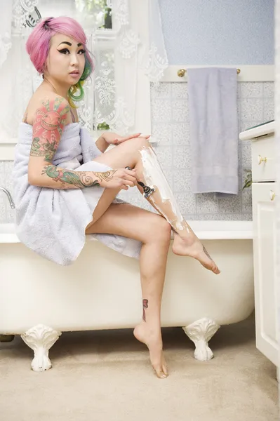 Женщина бреет ноги на боку ванны — стоковое фото