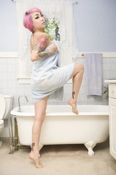 Ung kvinna i handduk poserar framför badkar — Stockfoto