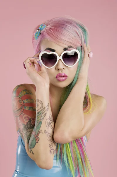 Ung kvinna poserar bär solglasögon över rosa bakgrund — Stockfoto