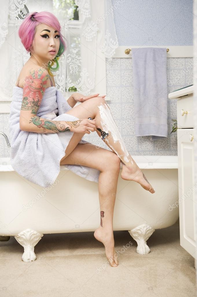 Woman shaving her legs on the side of the bathtub