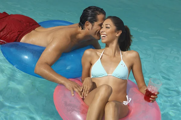 Casal em anéis infláveis sussurrando na piscina — Fotografia de Stock