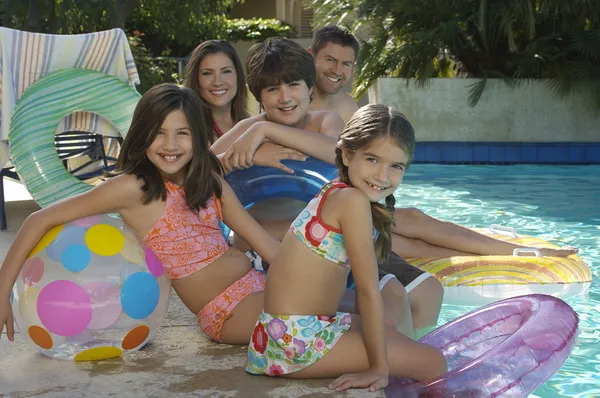 Família sentados juntos na beira da piscina — Fotografia de Stock