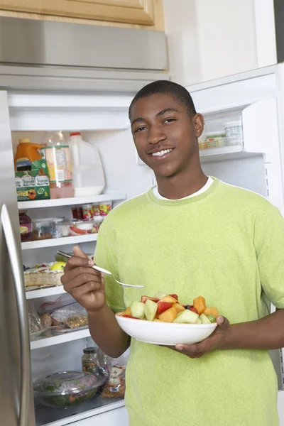 Niño comiendo ensalada por refrigerador abierto — Foto de Stock