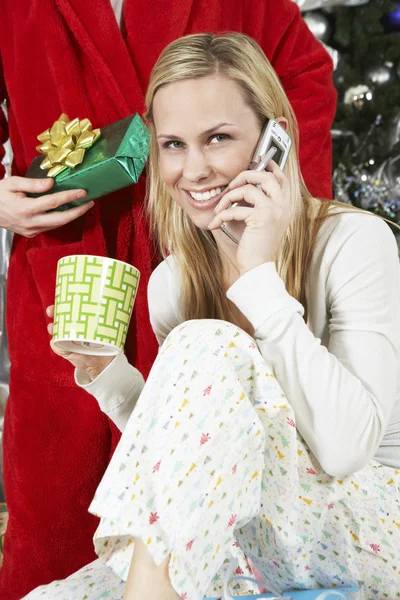 Vrouw met behulp van mobiele telefoon voor man met kerstcadeau — Stockfoto