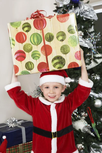 Boy In Santa Claus Outfit Carrying Present On Head — Stock Photo, Image