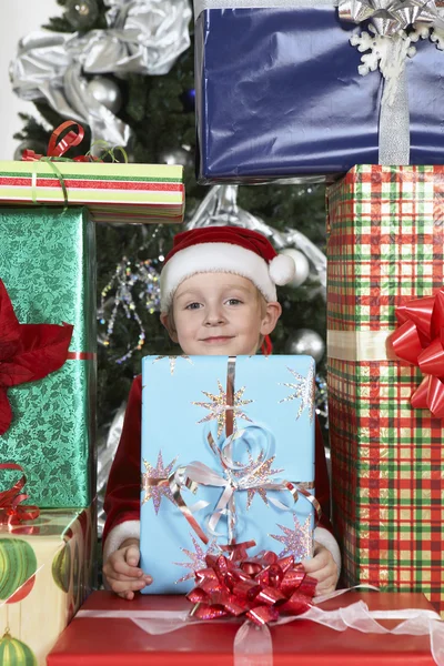 Söt pojke i santa hatt omgiven av presentförpackning — Stockfoto