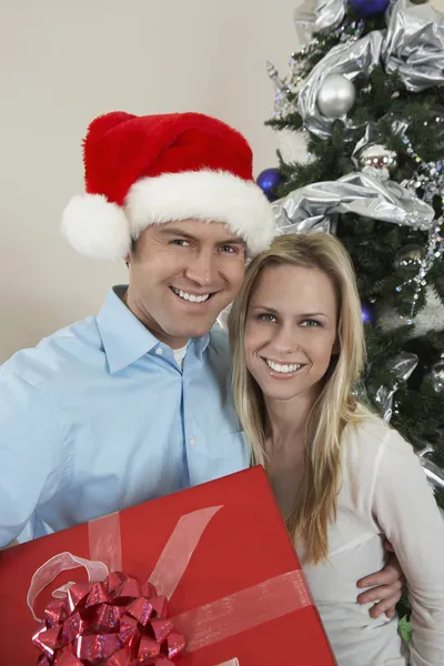 Pareja feliz con caja de regalo de pie junto al árbol de Navidad — Foto de Stock