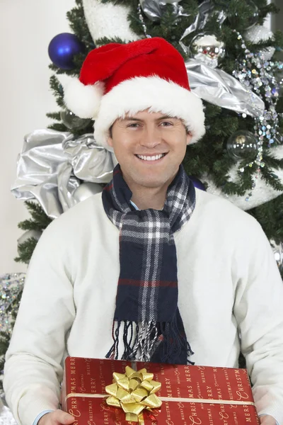 Man In Santa Cap Holding Gift Box By Christmas Tree — Stock Photo, Image