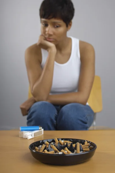 Женщина смотрит на полную пепельницу сигарет на столе — стоковое фото