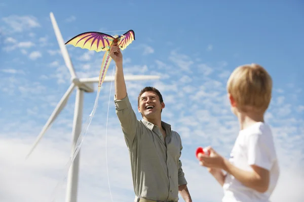 Far och son spelar med drake på vindkraftpark — Stockfoto
