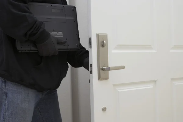 Ληστής κρατώντας το φορητό υπολογιστή, ενώ το άνοιγμα πόρτας του σπιτιού — Φωτογραφία Αρχείου