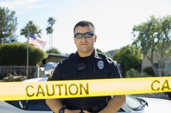 Офицер полиции, стоящий за лентой осторожности — стоковое фото