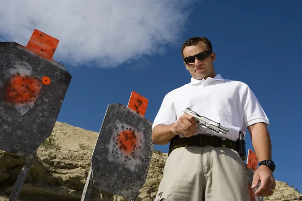 Hombre con pistola de mano cerca de objetivos en el campo de tiro — Foto de Stock