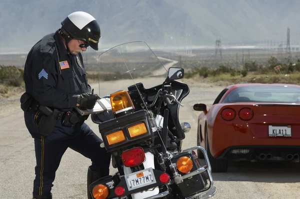 Дорожно-транспортный полицейский пишет против мотоцикла Лицензионные Стоковые Изображения