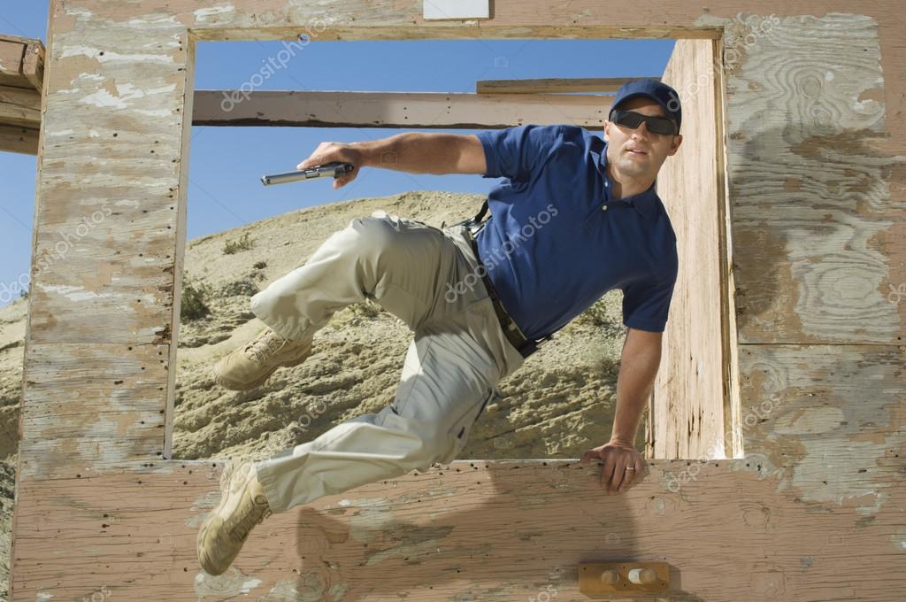Man With Hand Gun Jumping Obstacle At Firing Range Stock Photo by